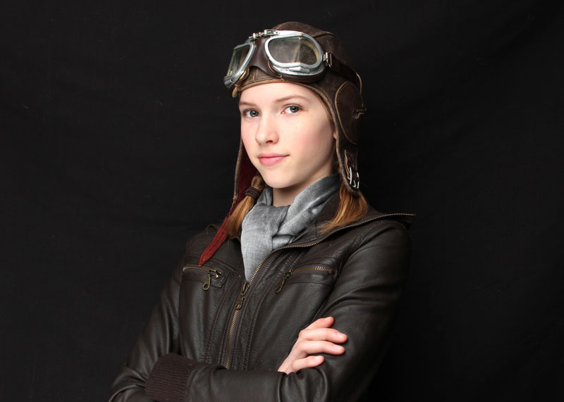 cies girl aviator in a brown leather bomber jacket, a gray scarf and a leather helmet folding her arms